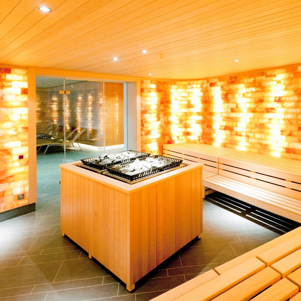 Moderne Sauna mit sanften Beleuchtungseffekten von himmelblauen Salzkristallen. Im Zentrum befindet sich ein Holztisch, umgeben von Bänken, die zum Entspannen einladen. Einladende Atmosphäre.