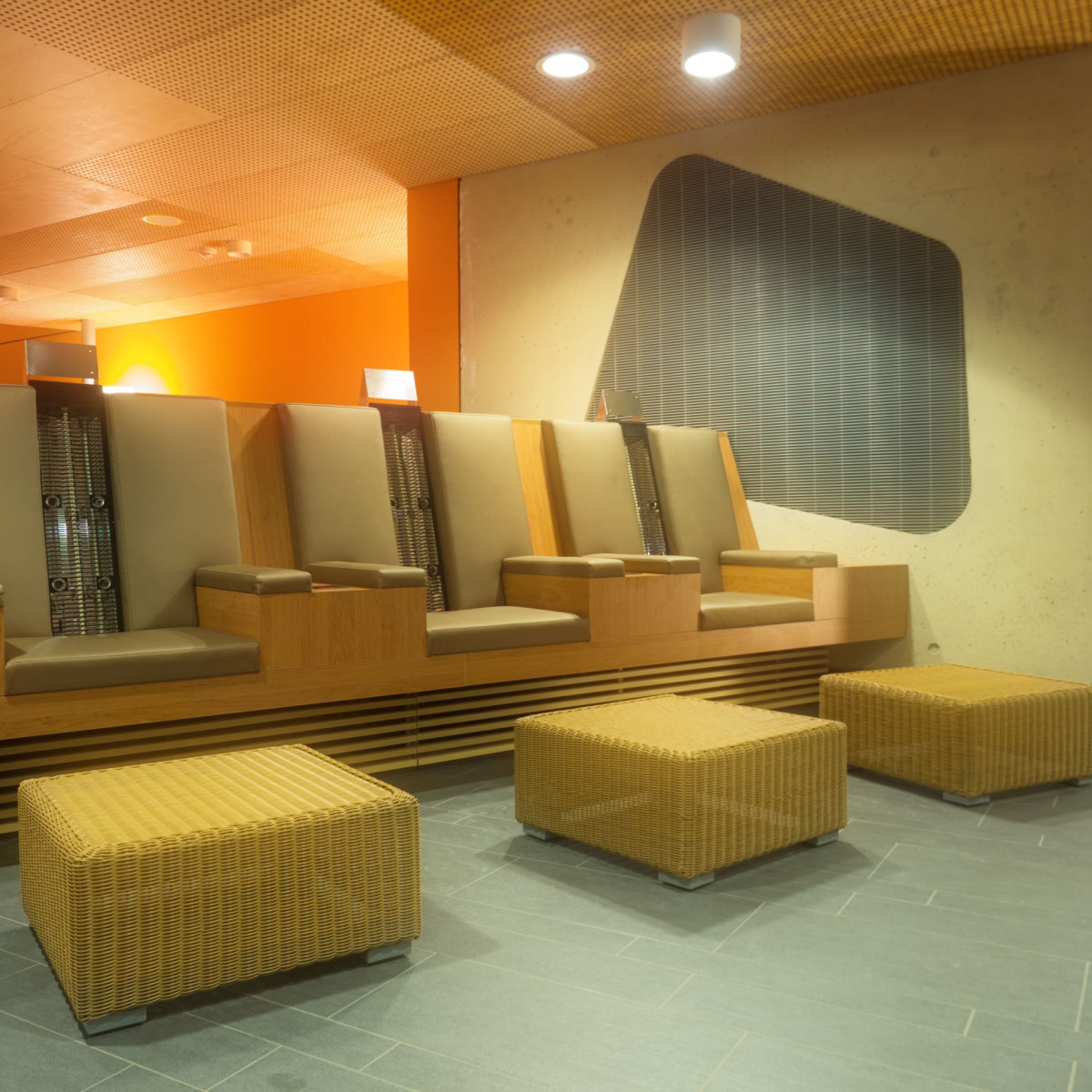 Modernes, minimalistisches Wartebereich mit eleganten, gepolsterten Sesseln aus Holz und stilvollen, geflochtenen Puffern in einem Raum mit warmen orangefarbenen Akzenten und sanfter Beleuchtung.