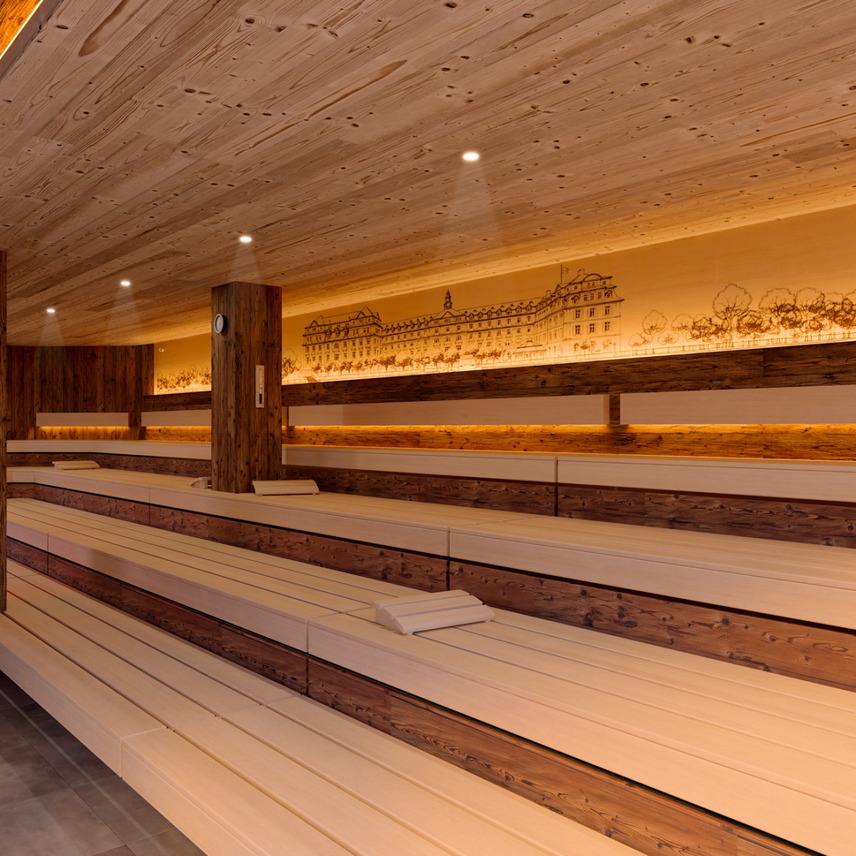Ein modernes, stilvolles Saunainneres mit Holzvertäfelung und sanfter Beleuchtung. Die Bänke sind aus hellem Holz, während eine dekorative Wand mit einer gezeichneten Architektur das Ambiente ergänzt.